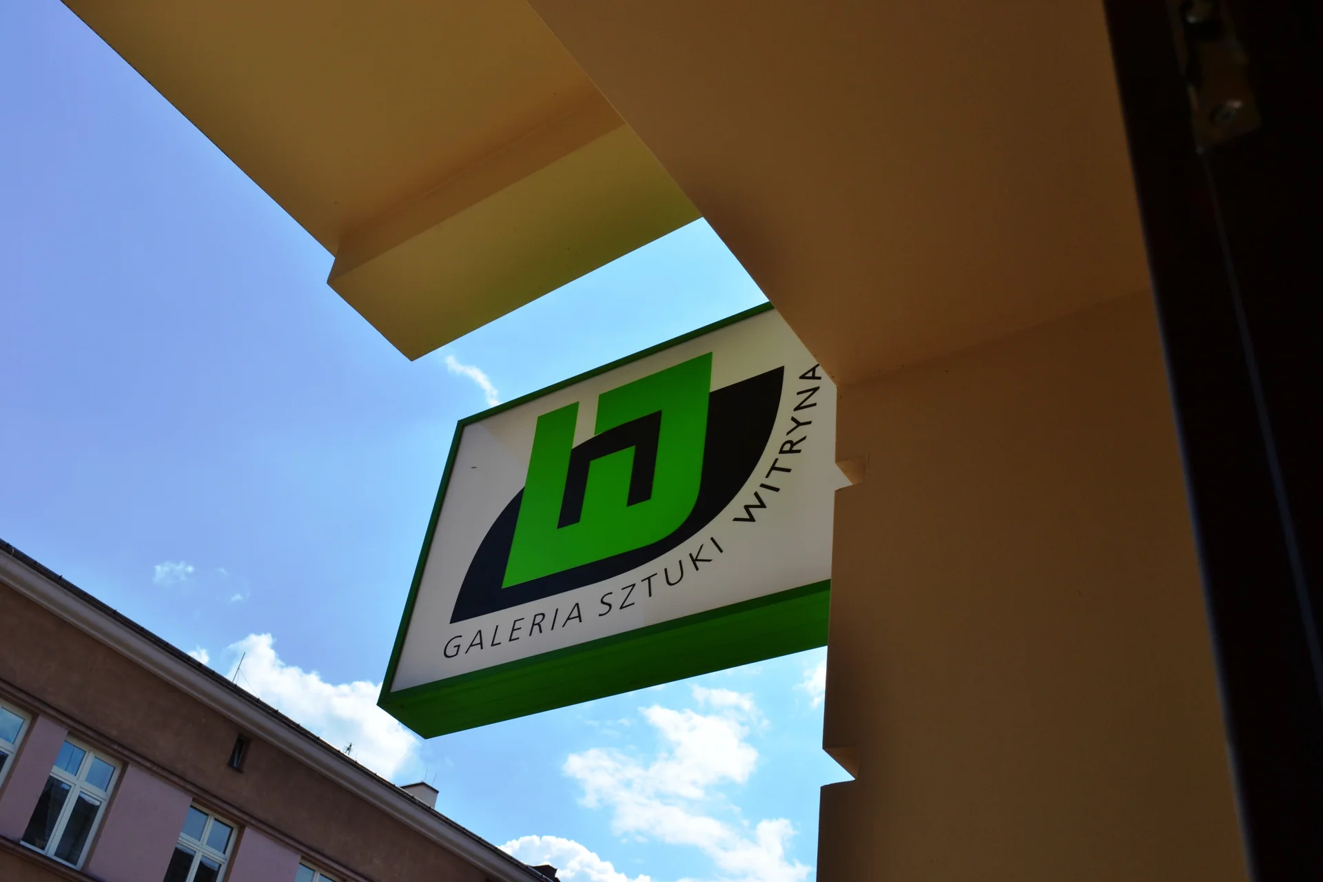 Zielony szyld Galerii Witryna na tle błękitnego nieba